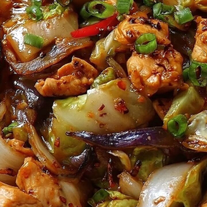 A white bowl filled with glossy, seared chicken and charred cabbage, garnished with fresh chopped scallions.