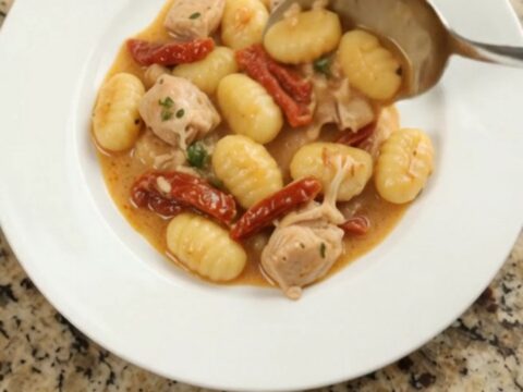 Creamy Parmesan chicken gnocchi in a slow cooker, topped with melted cheese and sun-dried tomatoes.