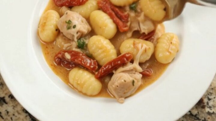 Creamy Parmesan chicken gnocchi in a slow cooker, topped with melted cheese and sun-dried tomatoes.