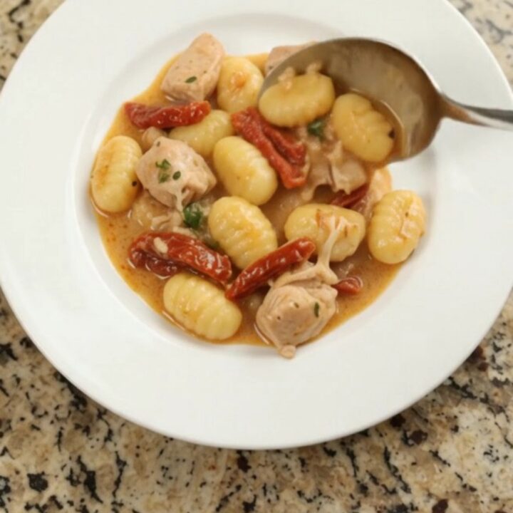 Creamy Parmesan chicken gnocchi in a slow cooker, topped with melted cheese and sun-dried tomatoes.