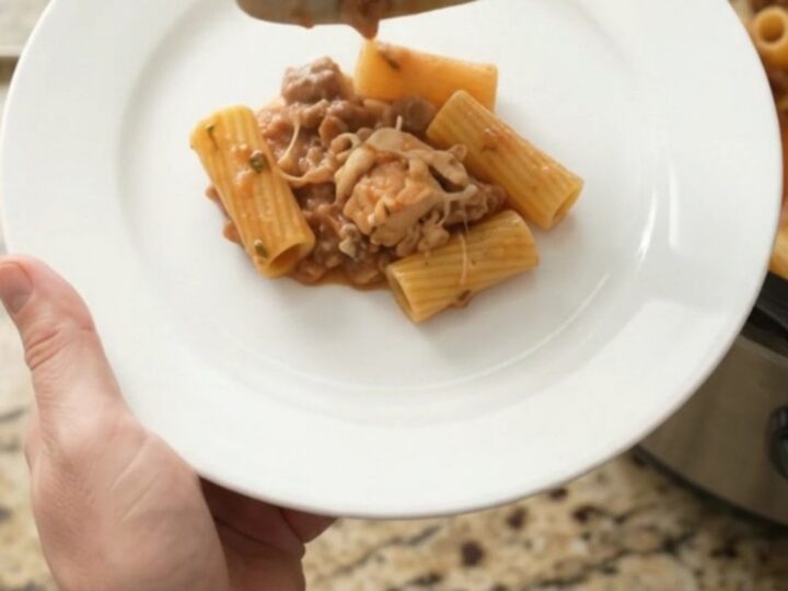 Slow cooker filled with creamy chicken rigatoni, topped with melted fontina and herbs.