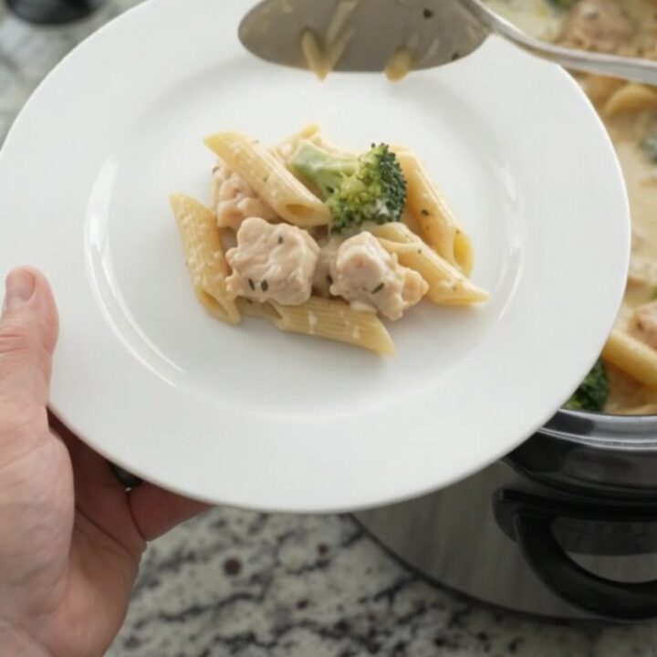 Slow cooker filled with creamy chicken Alfredo penne, topped with melted provolone and ricotta.
