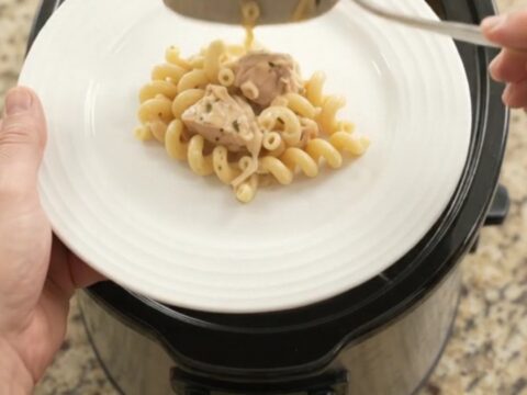 Creamy Crockpot Parmesan chicken cavatappi in a black slow cooker, topped with melted cheese and golden crust.