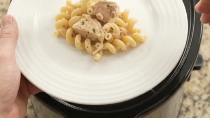 Creamy Crockpot Parmesan chicken cavatappi in a black slow cooker, topped with melted cheese and golden crust.