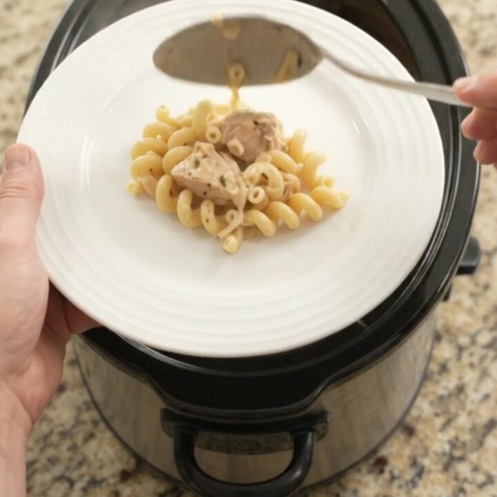 Creamy Crockpot Parmesan chicken cavatappi in a black slow cooker, topped with melted cheese and golden crust.