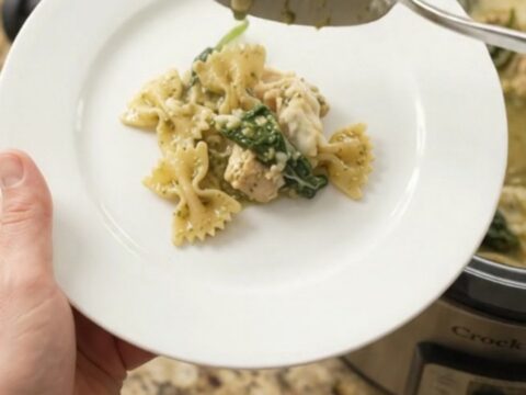 Creamy Crockpot chicken pesto farfalle with melted mozzarella and spinach, served in a white bowl