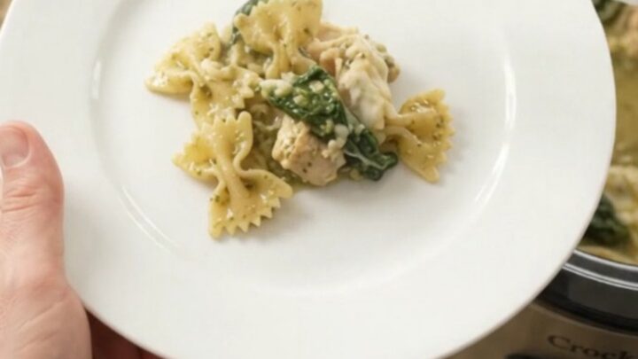 Creamy Crockpot chicken pesto farfalle with melted mozzarella and spinach, served in a white bowl