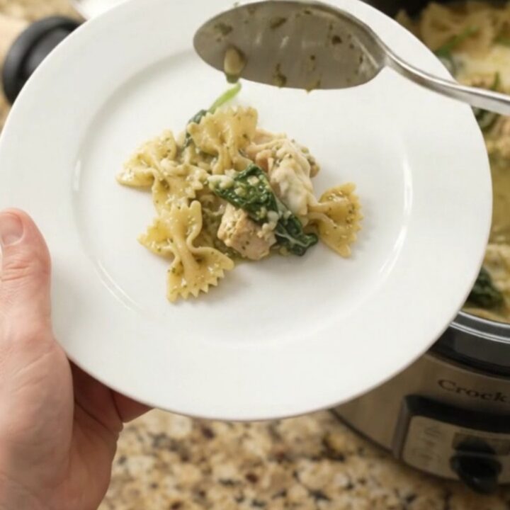 Creamy Crockpot chicken pesto farfalle with melted mozzarella and spinach, served in a white bowl