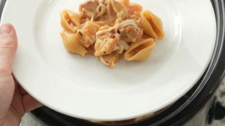 Slow cooker filled with creamy chicken and pasta shells topped with melted mozzarella, with steam rising