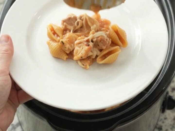 Slow cooker filled with creamy chicken and pasta shells topped with melted mozzarella, with steam rising