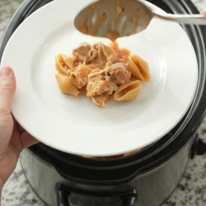 Slow cooker filled with creamy chicken and pasta shells topped with melted mozzarella, with steam rising