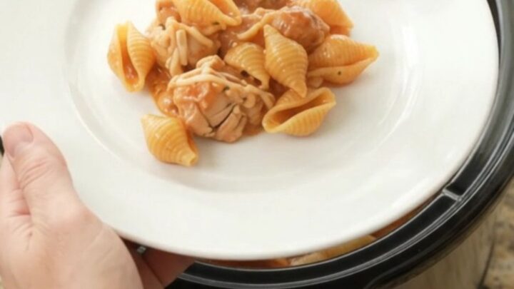 Slow cooker full of creamy Parmesan chicken red pepper shells, with golden melted cheese and steam rising.
