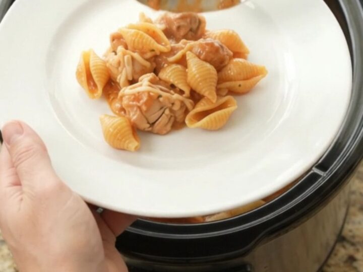 Slow cooker full of creamy Parmesan chicken red pepper shells, with golden melted cheese and steam rising.