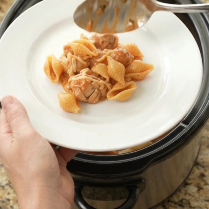 Slow cooker full of creamy Parmesan chicken red pepper shells, with golden melted cheese and steam rising.