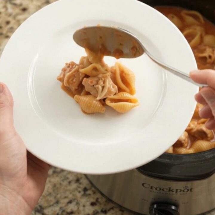 Slow cooker filled with creamy chicken and pasta shells topped with melted provolone.