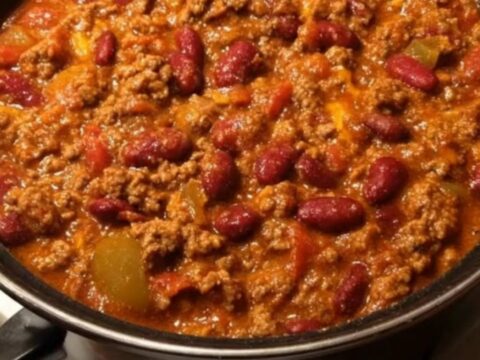A black pot filled with thick, bubbling beef and kidney bean chili simmering gently on a white stove.