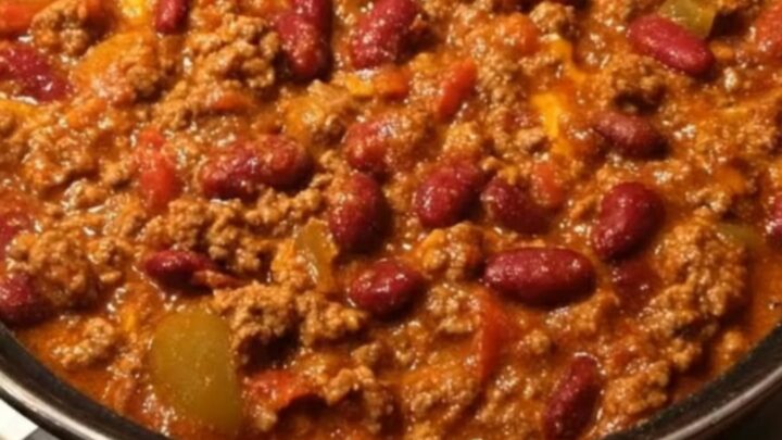 A black pot filled with thick, bubbling beef and kidney bean chili simmering gently on a white stove.