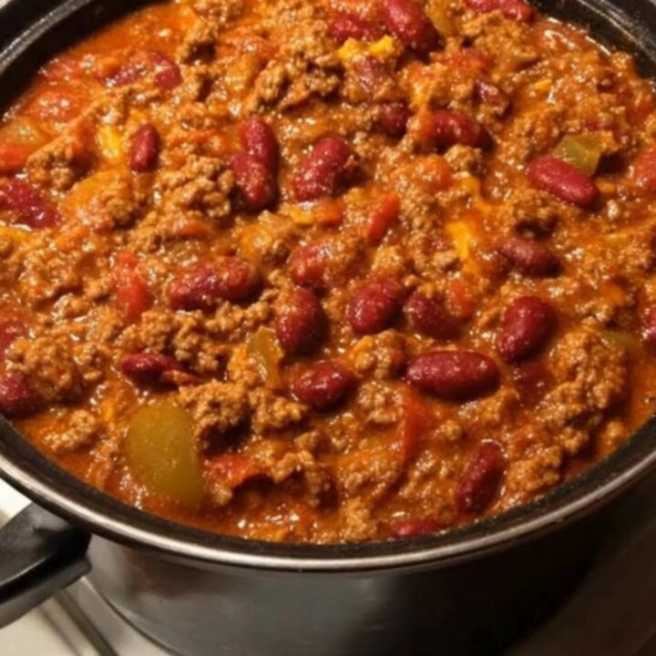 A black pot filled with thick, bubbling beef and kidney bean chili simmering gently on a white stove.