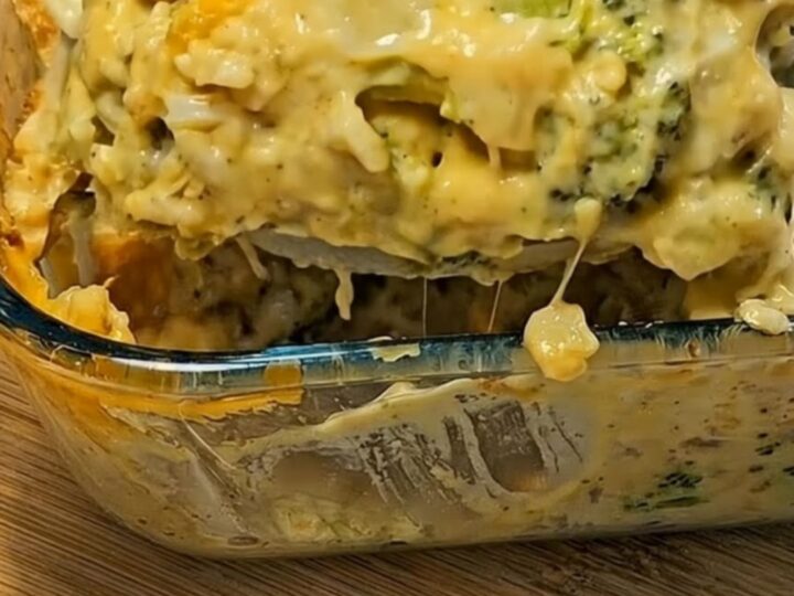 A large serving spoon lifting a creamy, piping-hot scoop of broccoli cheese casserole with melted cheese stretching downward