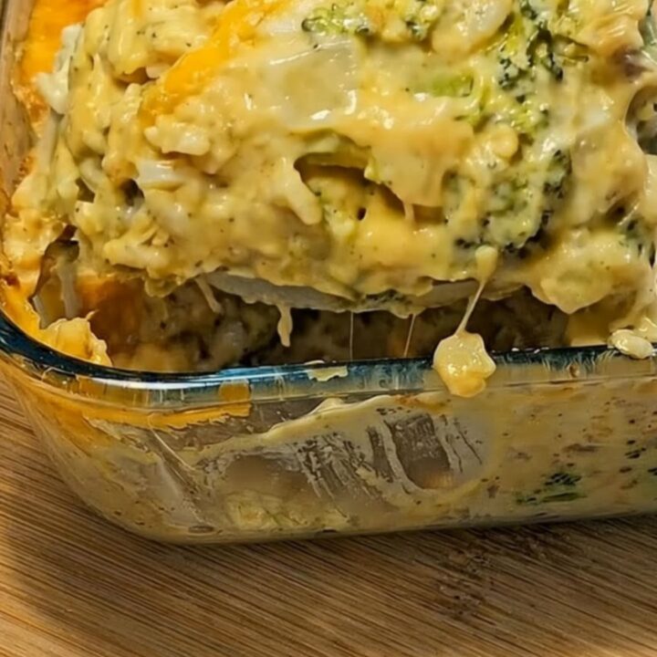 A large serving spoon lifting a creamy, piping-hot scoop of broccoli cheese casserole with melted cheese stretching downward