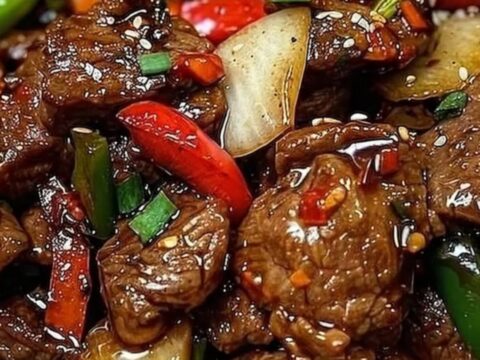 A close-up of sizzling black pepper beef with vibrant bell peppers on a dark plate.