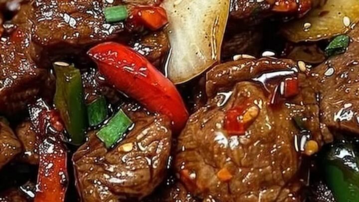 A close-up of sizzling black pepper beef with vibrant bell peppers on a dark plate.