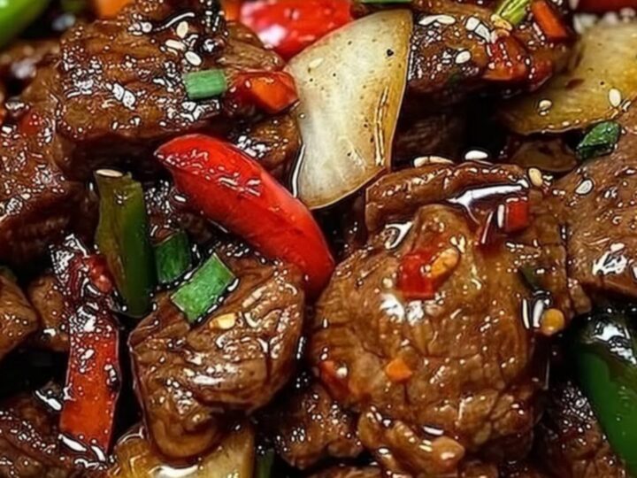 A close-up of sizzling black pepper beef with vibrant bell peppers on a dark plate.