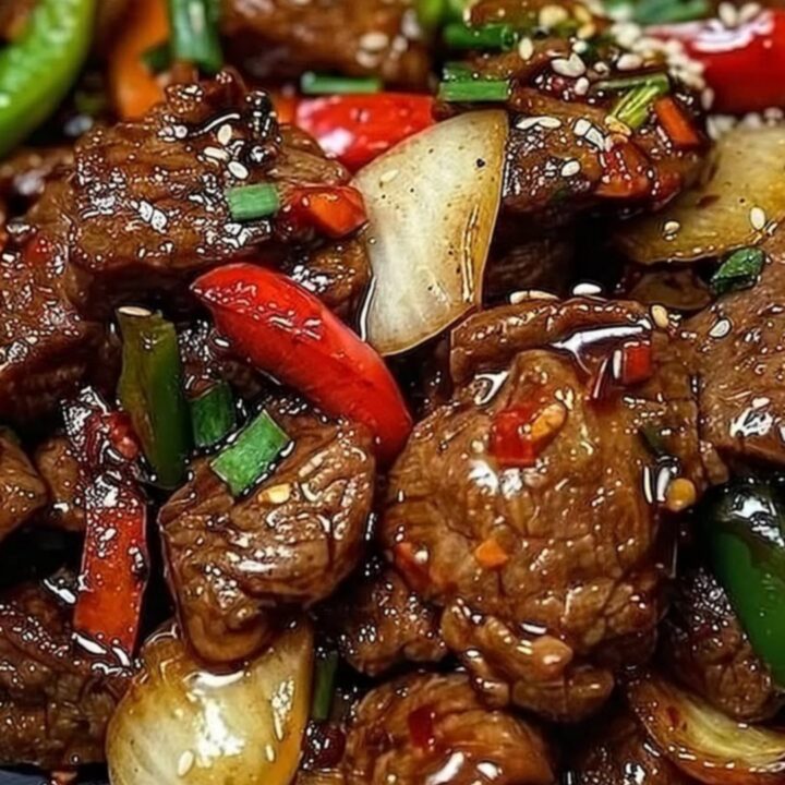 A close-up of sizzling black pepper beef with vibrant bell peppers on a dark plate.