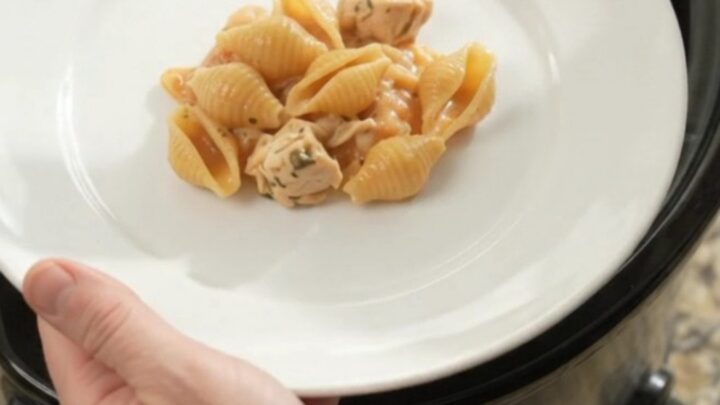 Slow cooker filled with creamy Boursin chicken red pepper shells pasta, topped with melted fontina and steam rising.