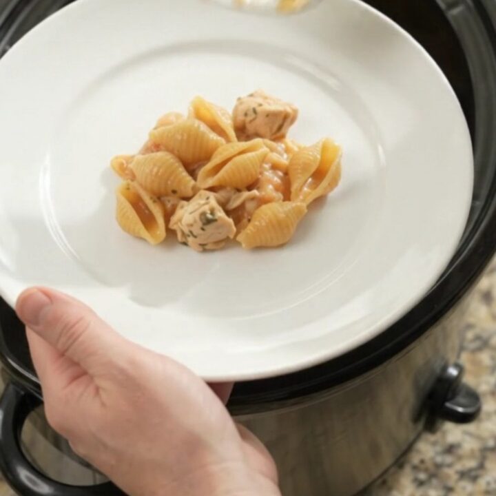 Slow cooker filled with creamy Boursin chicken red pepper shells pasta, topped with melted fontina and steam rising.
