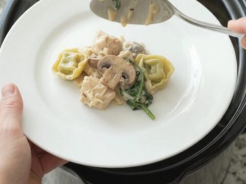Crockpot full of creamy Parmesan chicken spinach tortellini with melted cheese and steam rising
