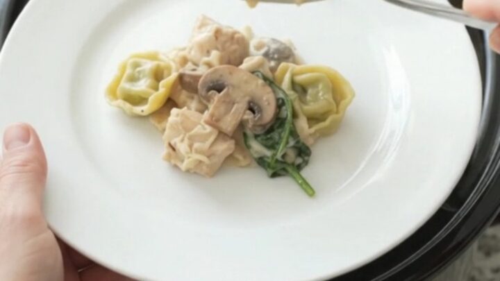 Crockpot full of creamy Parmesan chicken spinach tortellini with melted cheese and steam rising