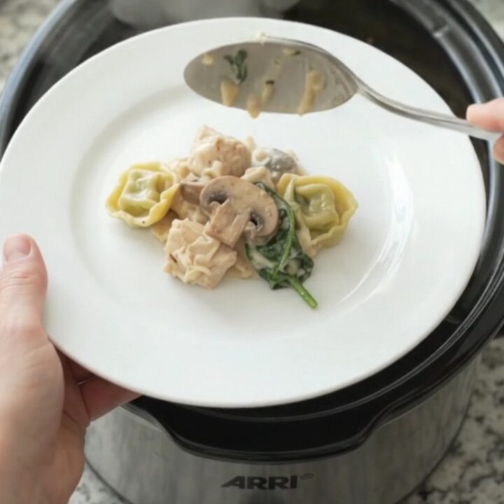 Crockpot full of creamy Parmesan chicken spinach tortellini with melted cheese and steam rising