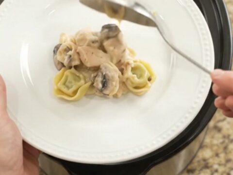 Slow cooker filled with creamy chicken spinach tortellini Alfredo, topped with melted provolone and ricotta.