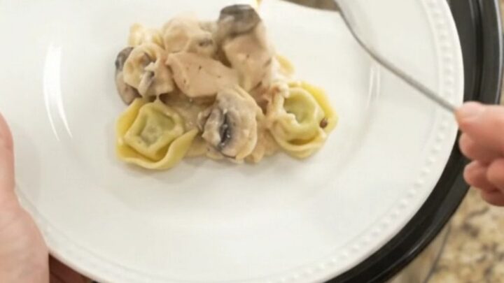 Slow cooker filled with creamy chicken spinach tortellini Alfredo, topped with melted provolone and ricotta.