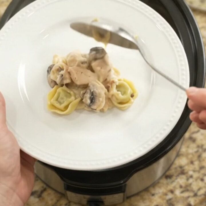 Slow cooker filled with creamy chicken spinach tortellini Alfredo, topped with melted provolone and ricotta.