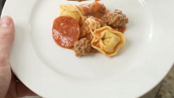 Slow cooker filled with cheesy tortellini, sausage, and pepperoni, bubbling hot