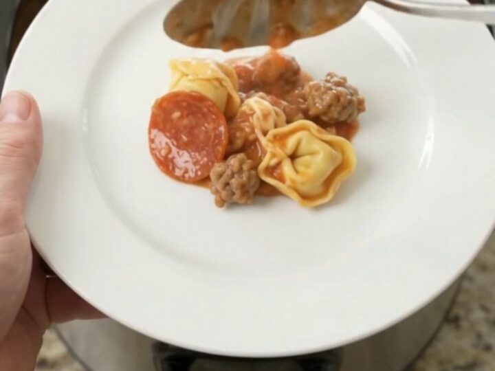 Slow cooker filled with cheesy tortellini, sausage, and pepperoni, bubbling hot