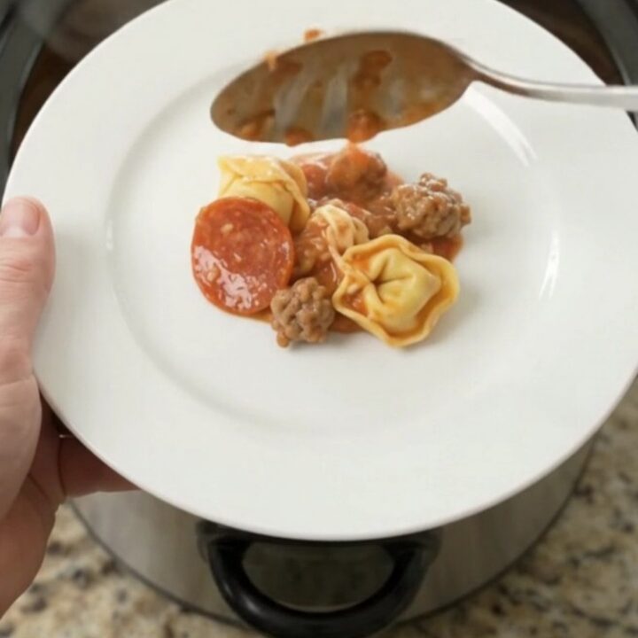 Slow cooker filled with cheesy tortellini, sausage, and pepperoni, bubbling hot
