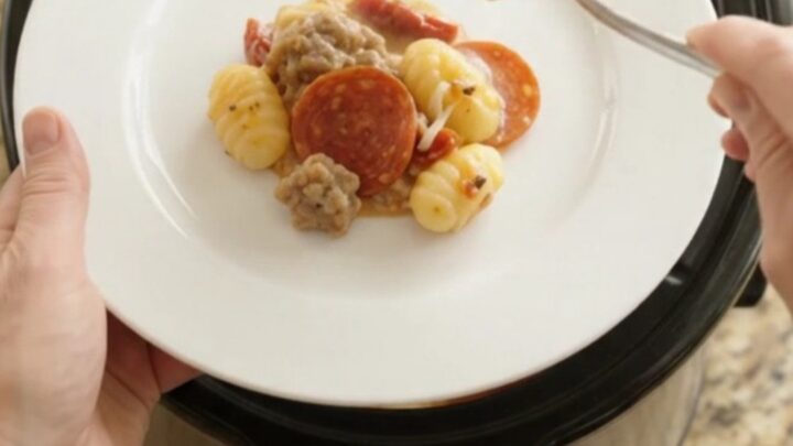 Slow cooker filled with creamy pepperoni sausage gnocchi, topped with melted mozzarella and steam rising.