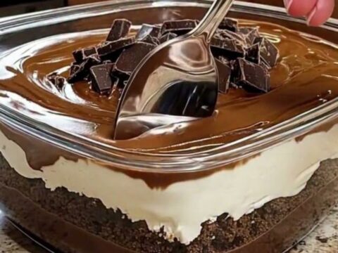 A close-up of a glass dish filled with layers of chocolate pudding and cream, topped with chocolate chunks.
