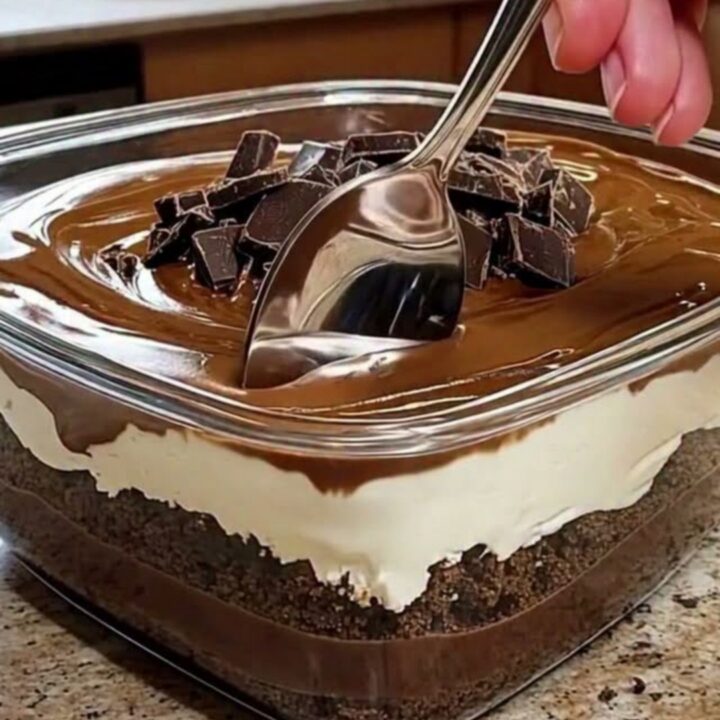 A close-up of a glass dish filled with layers of chocolate pudding and cream, topped with chocolate chunks.
