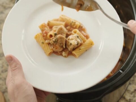A slow cooker filled with creamy Boursin chicken baked ziti, with melted cheese and herbs on top.