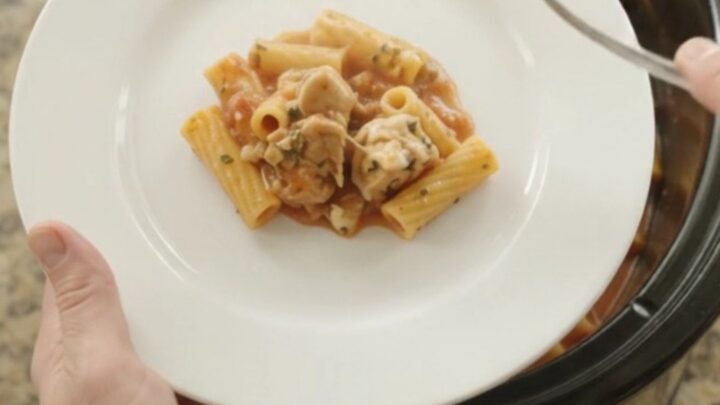 A slow cooker filled with creamy Boursin chicken baked ziti, with melted cheese and herbs on top.