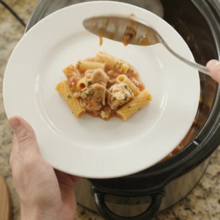 A slow cooker filled with creamy Boursin chicken baked ziti, with melted cheese and herbs on top.