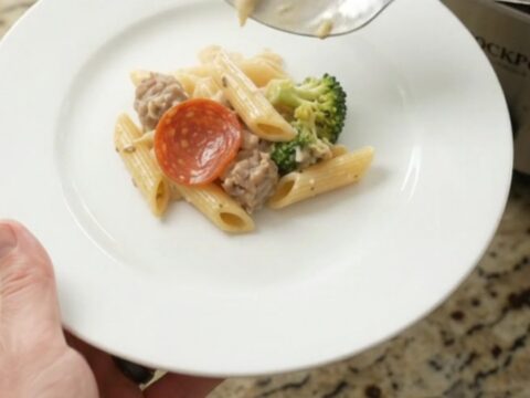 Slow cooker filled with creamy penne pasta, Italian sausage, pepperoni, and broccoli in Alfredo sauce with melted mozzarella