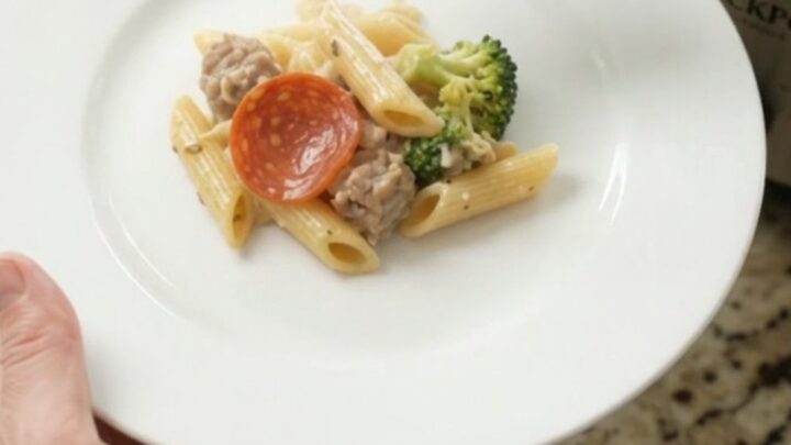Slow cooker filled with creamy penne pasta, Italian sausage, pepperoni, and broccoli in Alfredo sauce with melted mozzarella