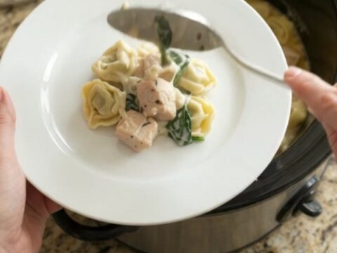 Creamy Crockpot Boursin chicken tortellini in a black slow cooker, topped with melted fontina and herbs.