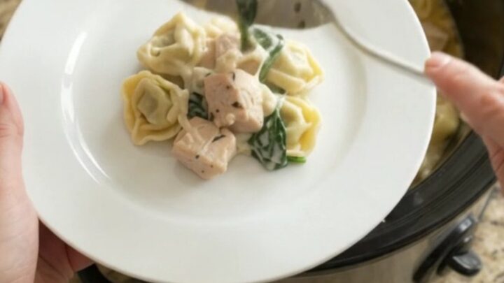 Creamy Crockpot Boursin chicken tortellini in a black slow cooker, topped with melted fontina and herbs.