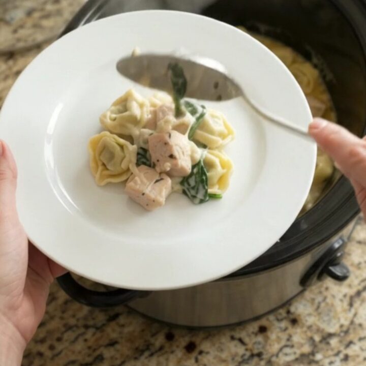 Creamy Crockpot Boursin chicken tortellini in a black slow cooker, topped with melted fontina and herbs.